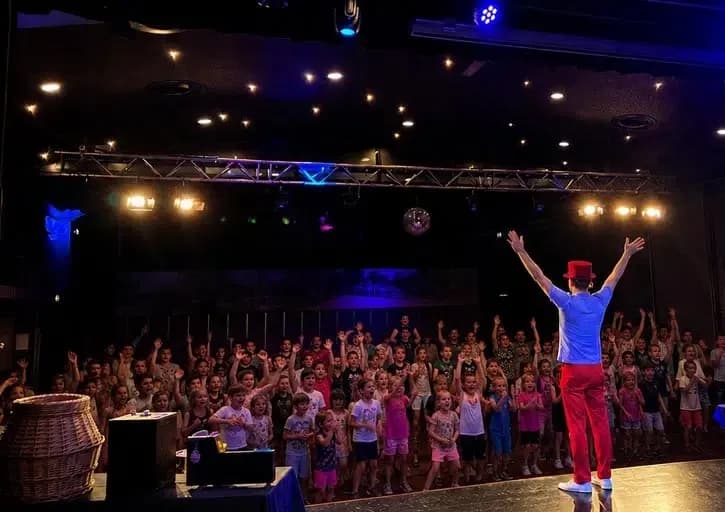 Pieter voor een theaterzaal met enthousiast meedoende kinderen
