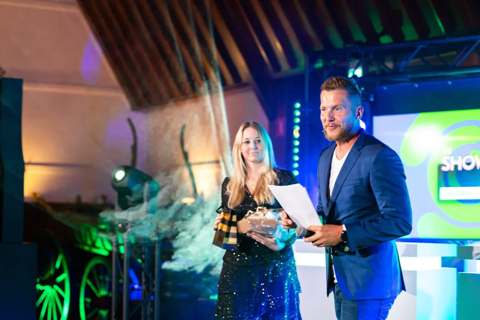 Presentator met microfoon en assistente tijdens De Bedrijfsborrel Show op locatie